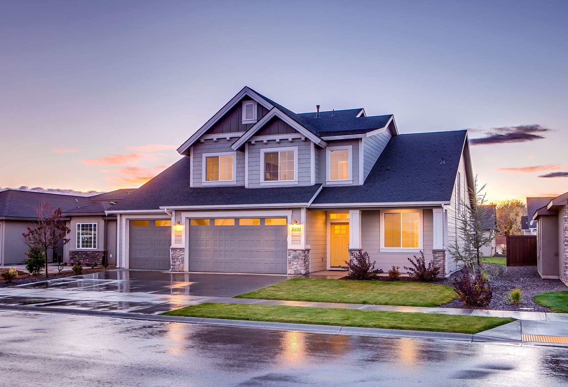 A two-story craftsman-style home at dusk with a wet driveway
