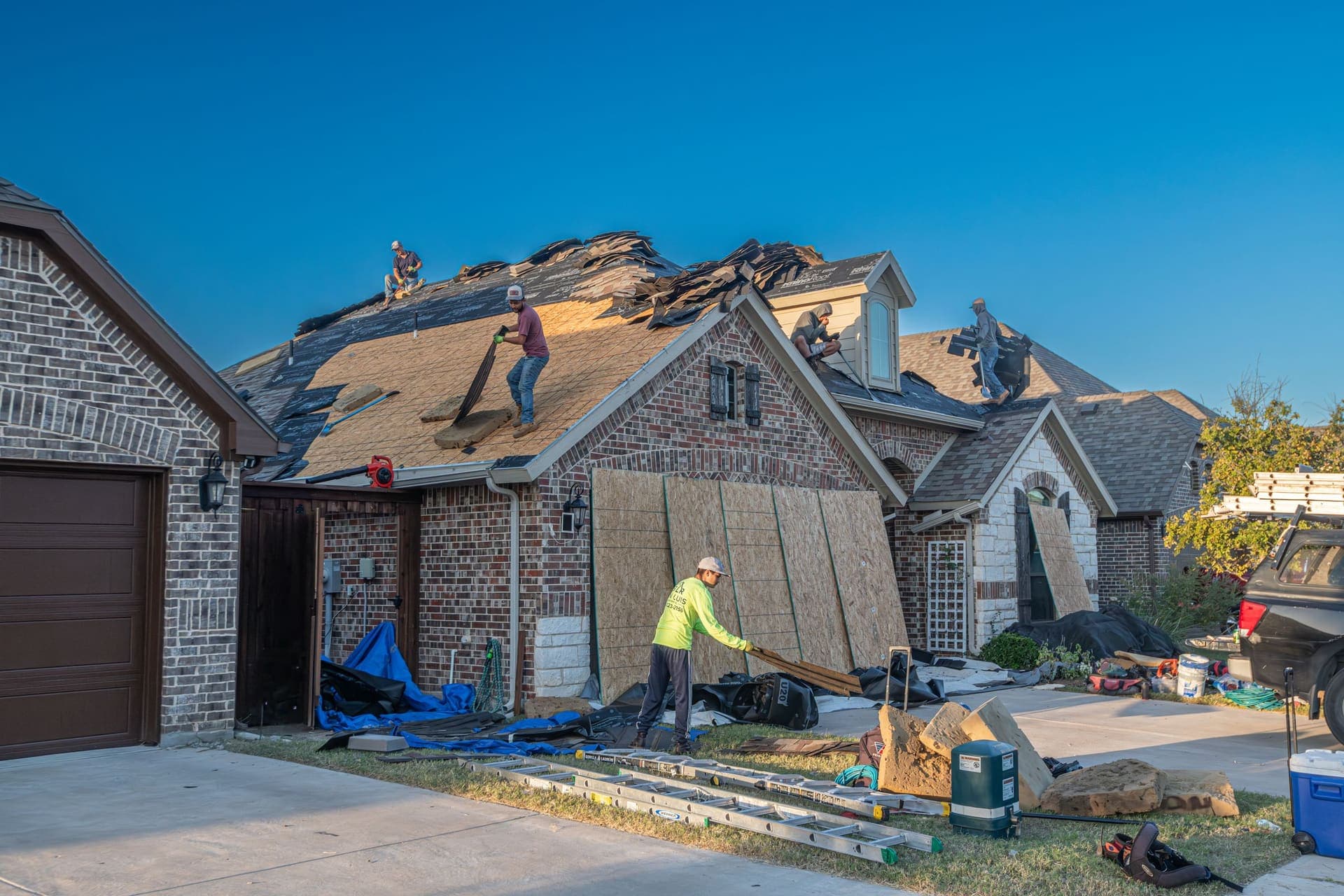 A crew tearing off and re-roofing a house, with old shingles stacked on the slope