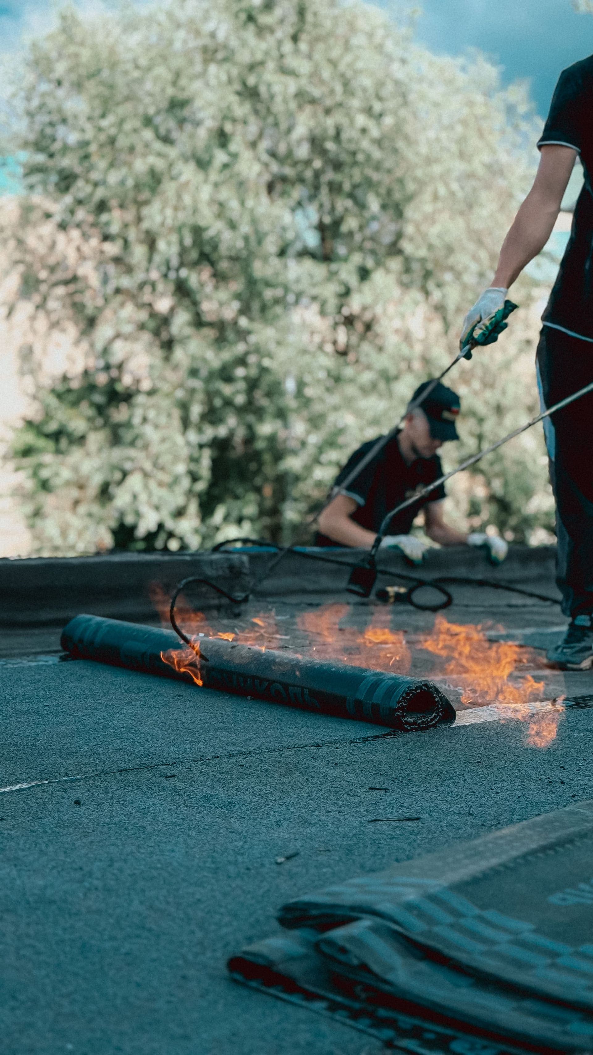 A roofer torch-applying a rolled membrane on a flat, low-slope roof