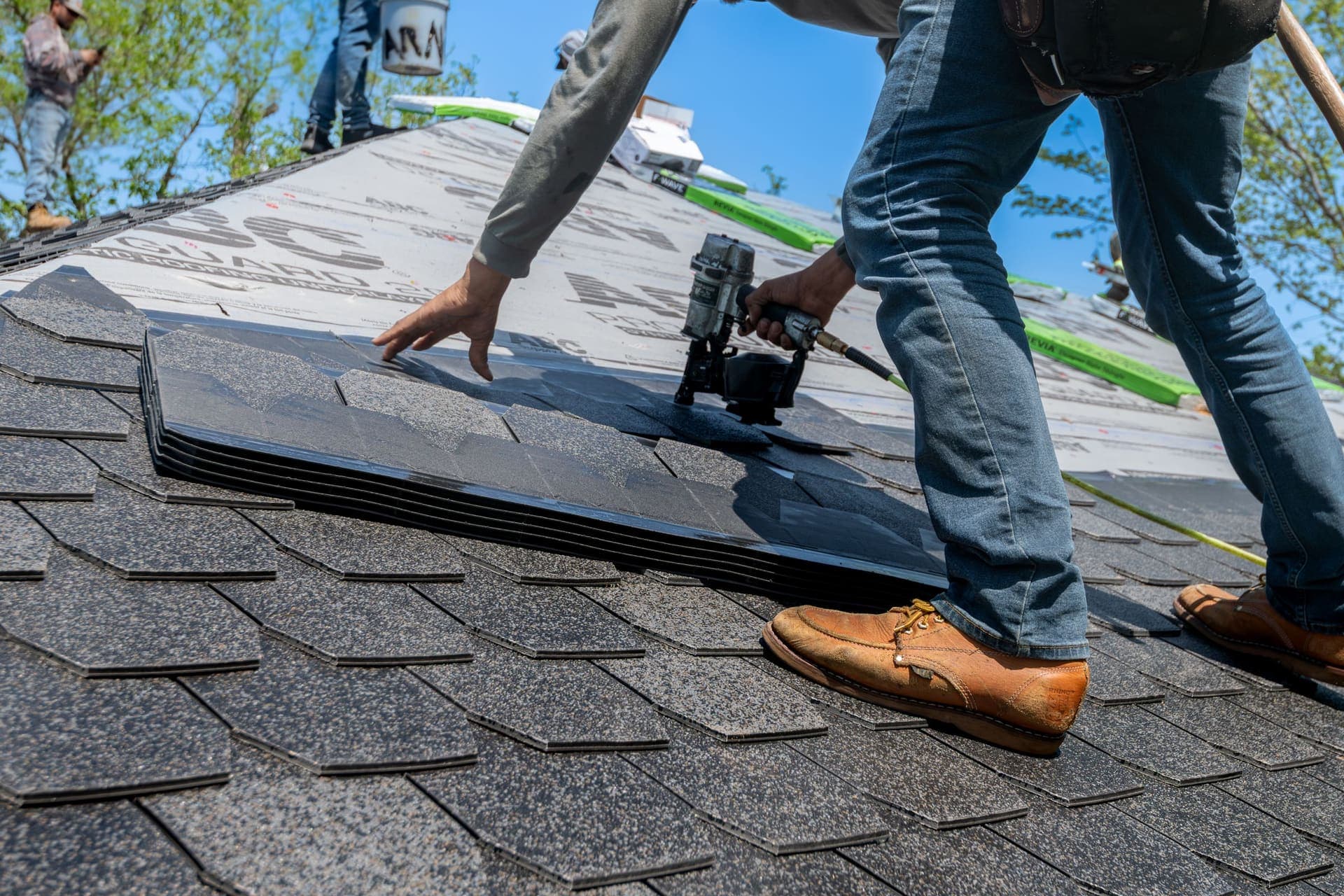 Close-up of a roofer's hands nailing down new asphalt shingles